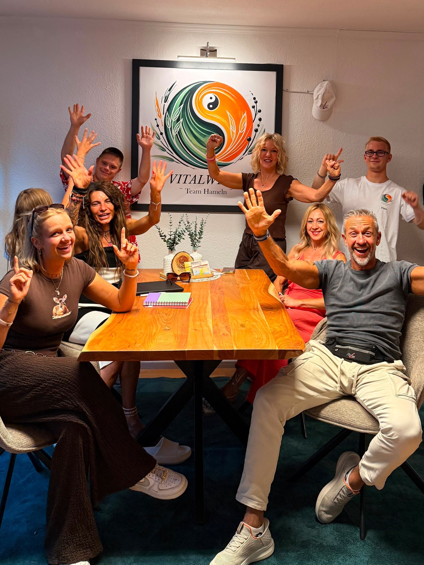 Das VitalWelt Team Hameln in der Baustraße 8: das Team jubelt um den Beratungstisch unter dem gerahmten VitalWelt-Logo